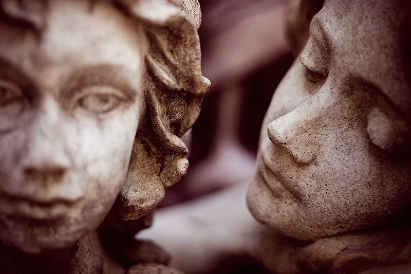 Two stone statues: one stoic, the other gazing at the first.