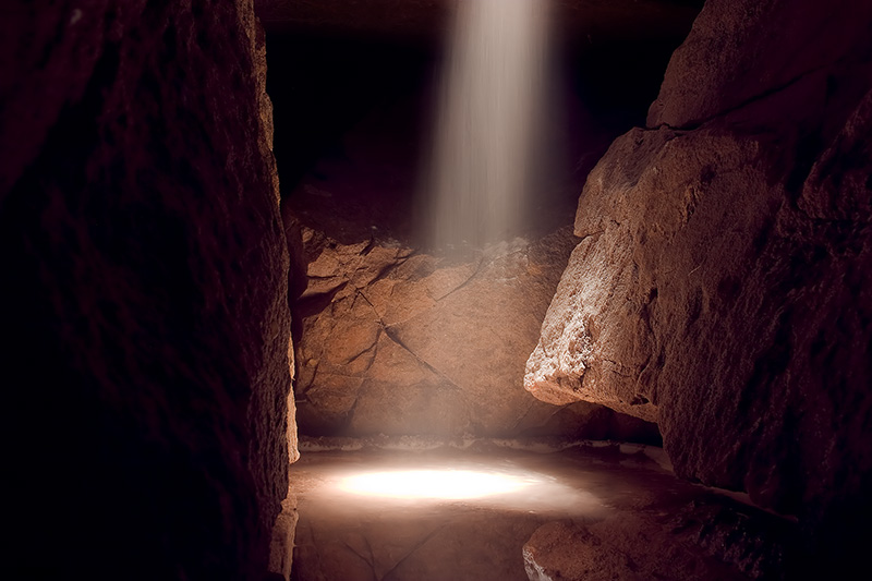 A shaft of light pierces through the darkness, revealing a small cove inside a cavern.