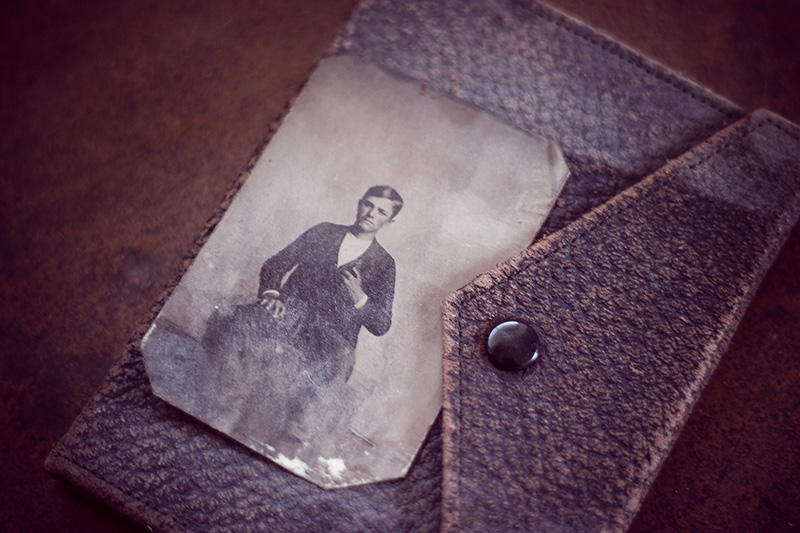 An antique tintype of a boy, sitting atop a closed leather photo album.