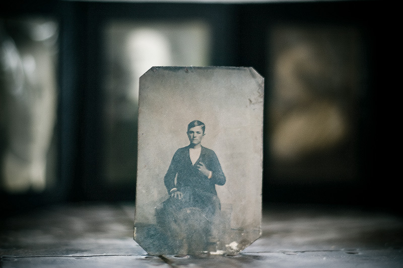 A tintype portrait of a boy, surrounded by other, distant, out-of-focus photographs.