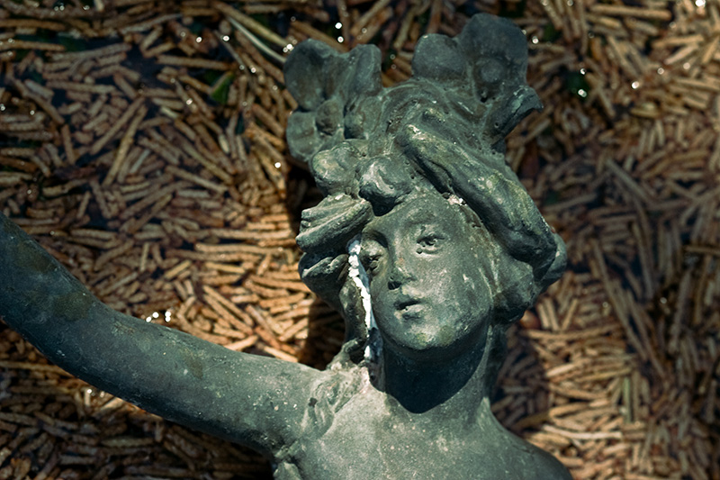 A bronze figurine of a tired-looking woman with one arm raised.