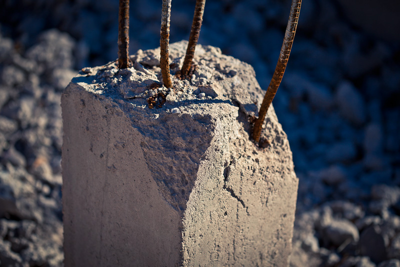 A concrete pillar with four shafts of bent, rusted rebar protruding vertically from it.