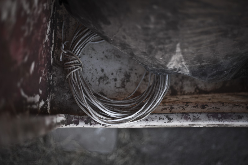 A coil of wire under a black garbage bag inside a paint-stained booth.