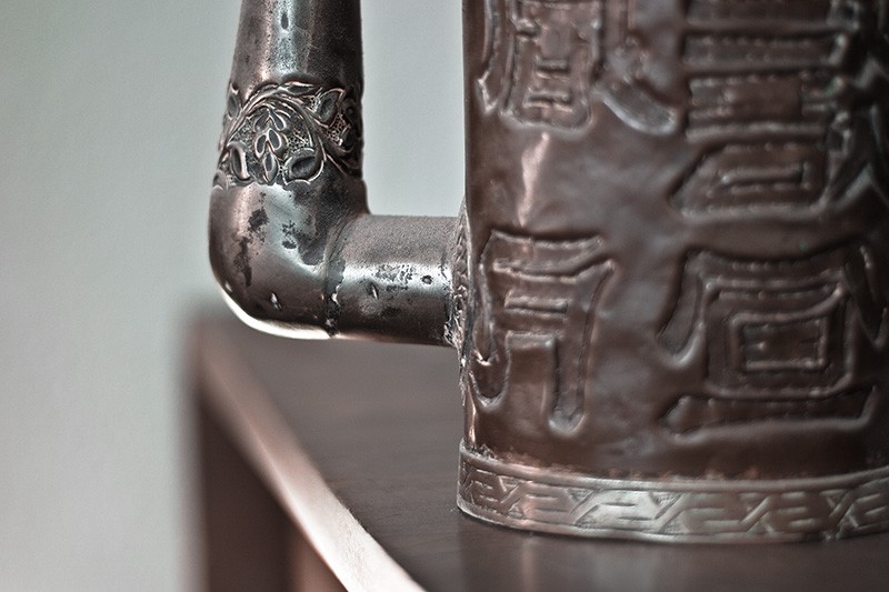A decorative band around the spout of a copper pitcher.
