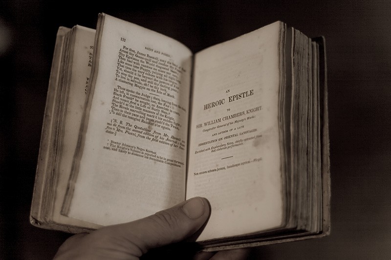 A hand holding open an old book of poetry.