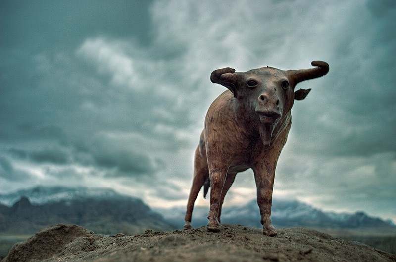 A leather sculpture of a bull-like animal stands against a backdrop of mountains and storm clouds.