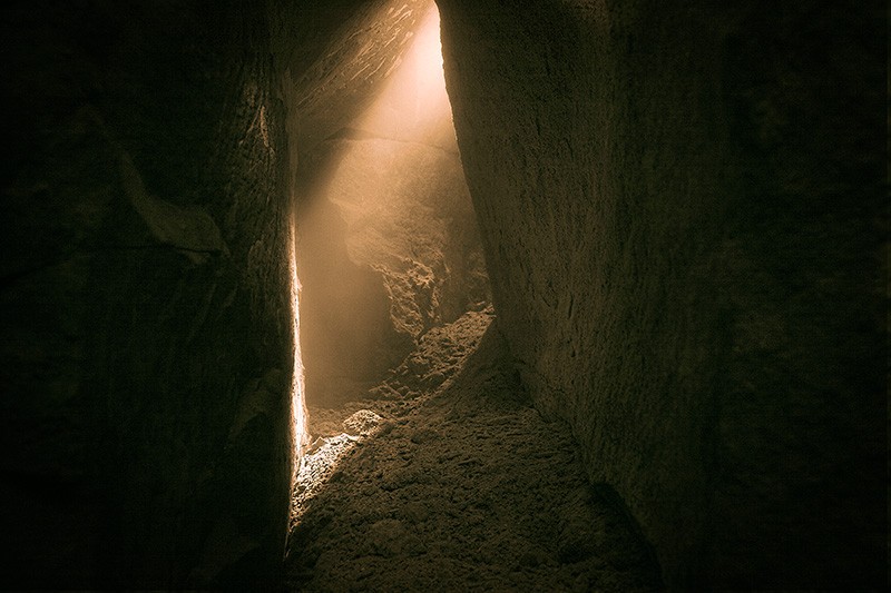 Light coming from a gap in the rock inside a cavern corridor.
