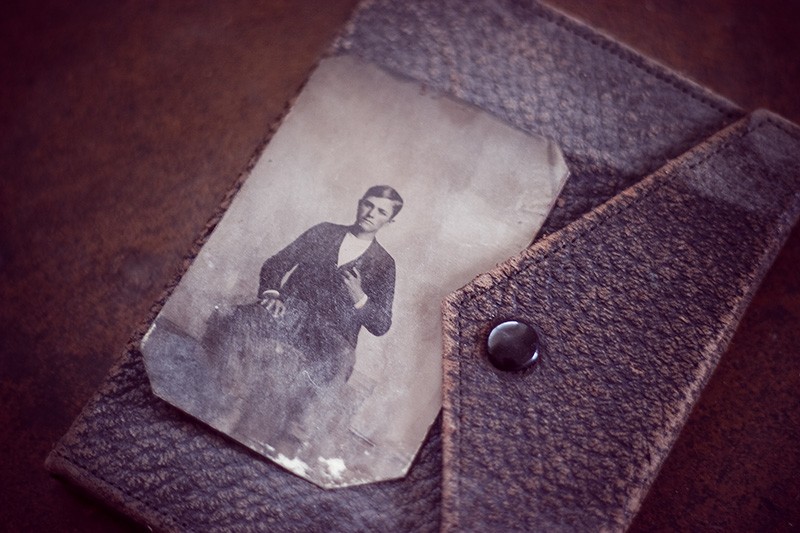 An antique tintype of a boy, sitting atop a closed leather photo album.