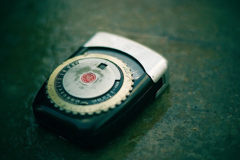 An old photographic light meter sitting on a wet cement surface.