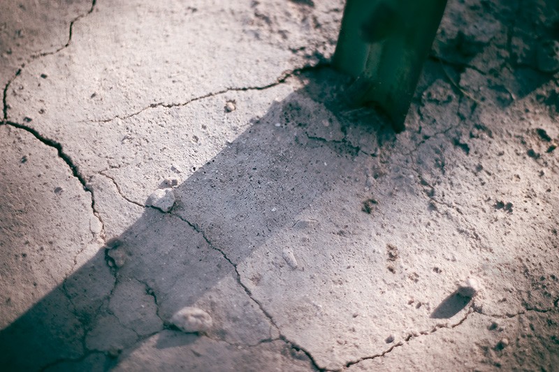 The shadow of a steel fence post, cast across cracked, dry earth.