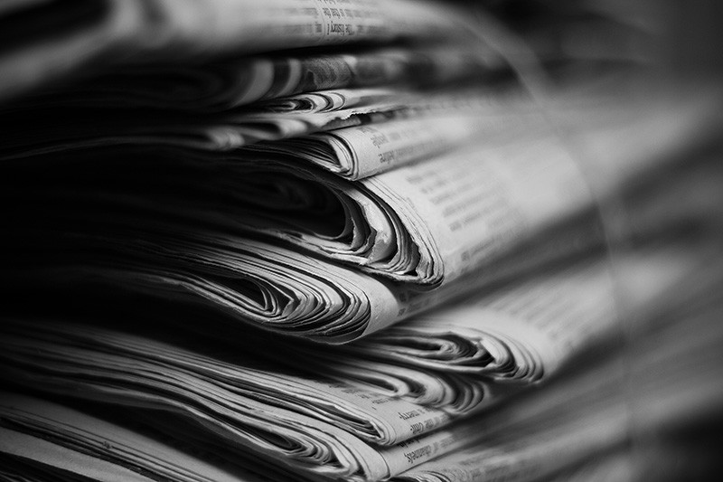 Numerous newspapers stacked and tied into a bundle.