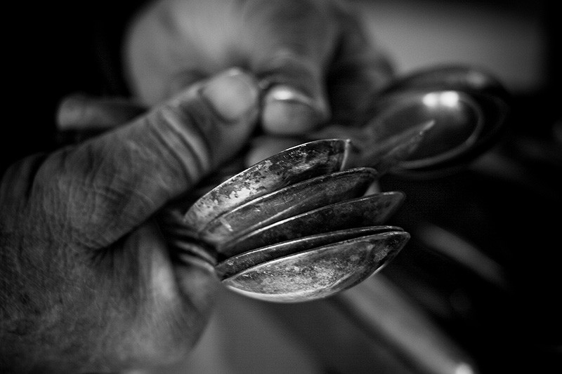Two hands holding numerous old spoons.