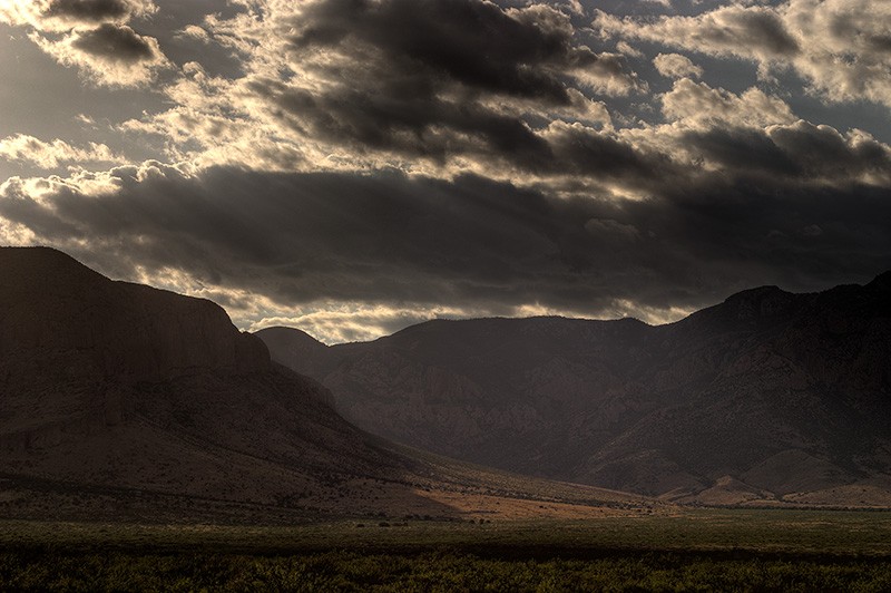 Sunlight shining through clouds above the entrance of a canyon.