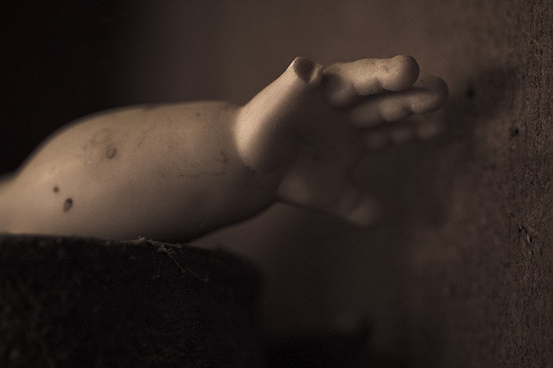 A doll arm with a missing little finger reaching out of a container.