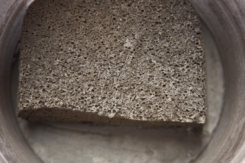 A dirty, dry sponge sitting in an equally dry bucket.