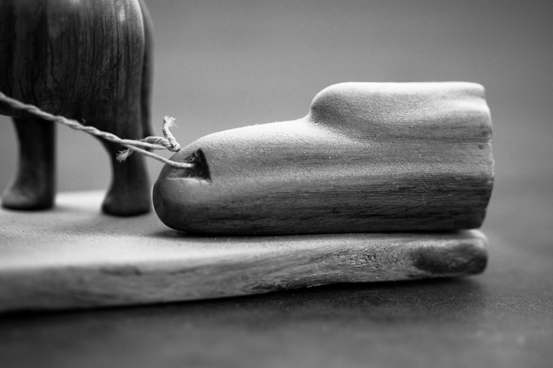 A miniature wooden elephant dragging a miniature piece of wood.