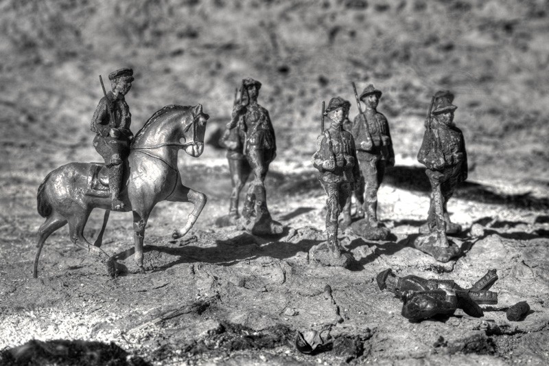 Soldiers on a burned-out battlefield march past dead bodies.