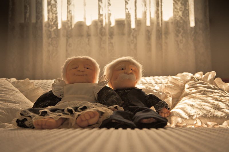 Two elderly dolls lying in bed, backlight by warm sunlight.