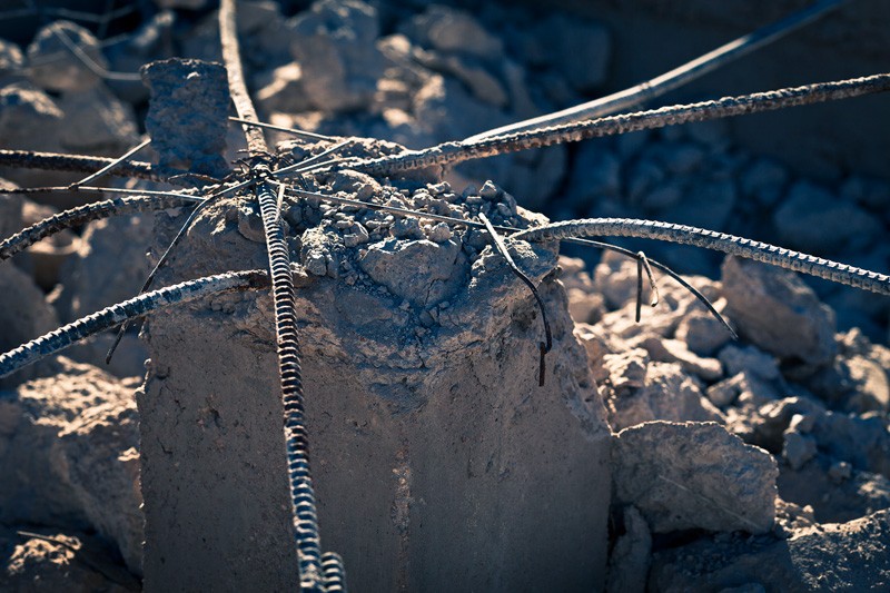 A crumbled cement pillar with rebar coming out the top and debris everywhere.