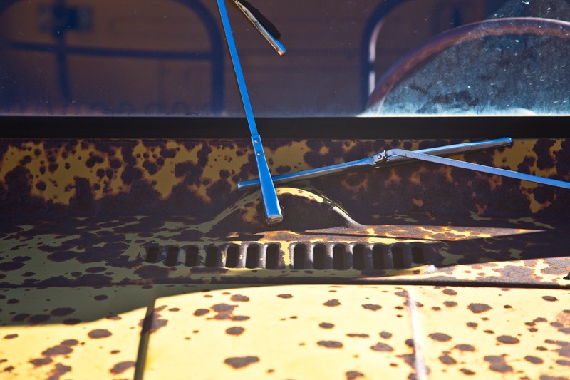 The windshield of an antique truck, with one of the windshield wipers fallen and out of position.