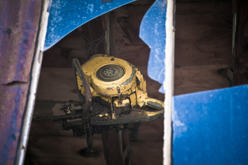 An antique chainsaw hangs from the rafters, viewed through a broken window.
