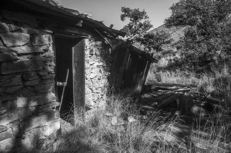 A figure standing in the doorway of an abandoned cabin, brandishing a walking stick.