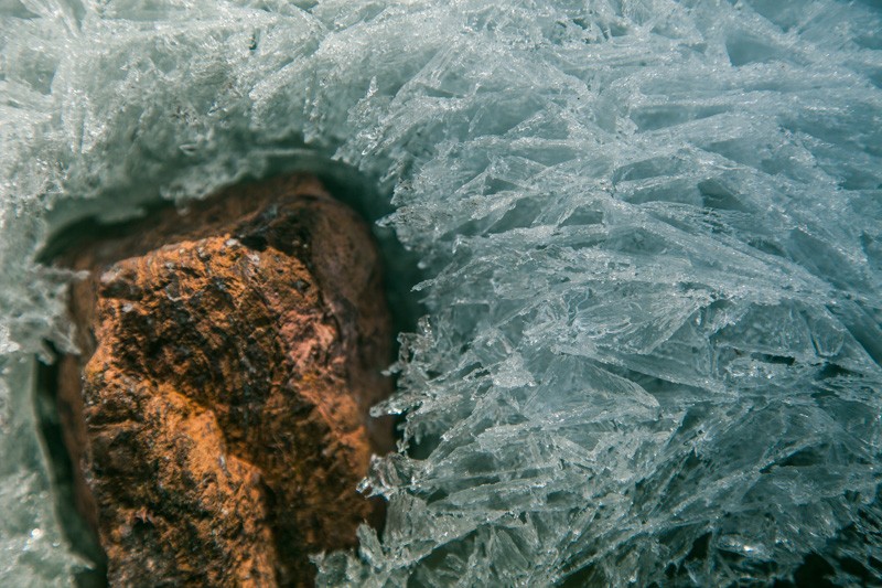 A red rock with patterned ice formed around it, a small gap between.