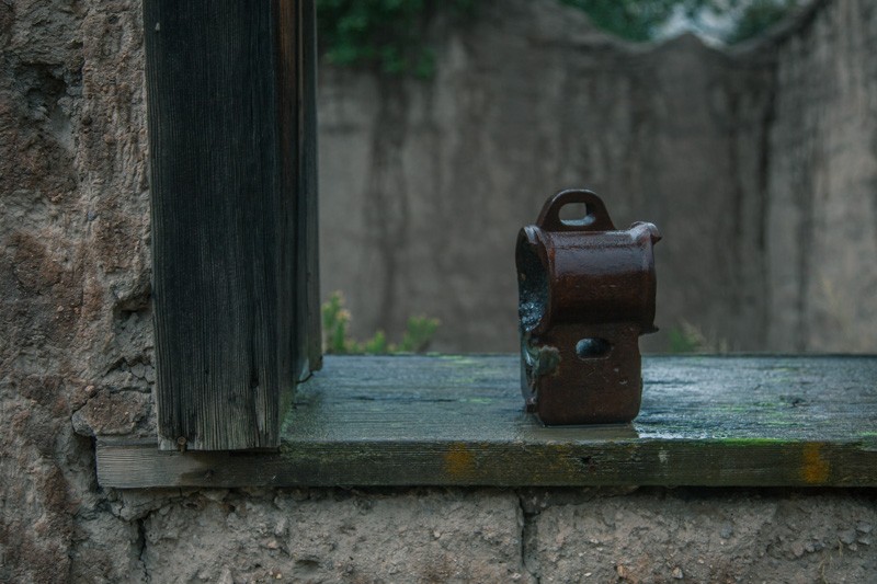 A broken part of an old machine on the windowsill of an abandoned adobe house.